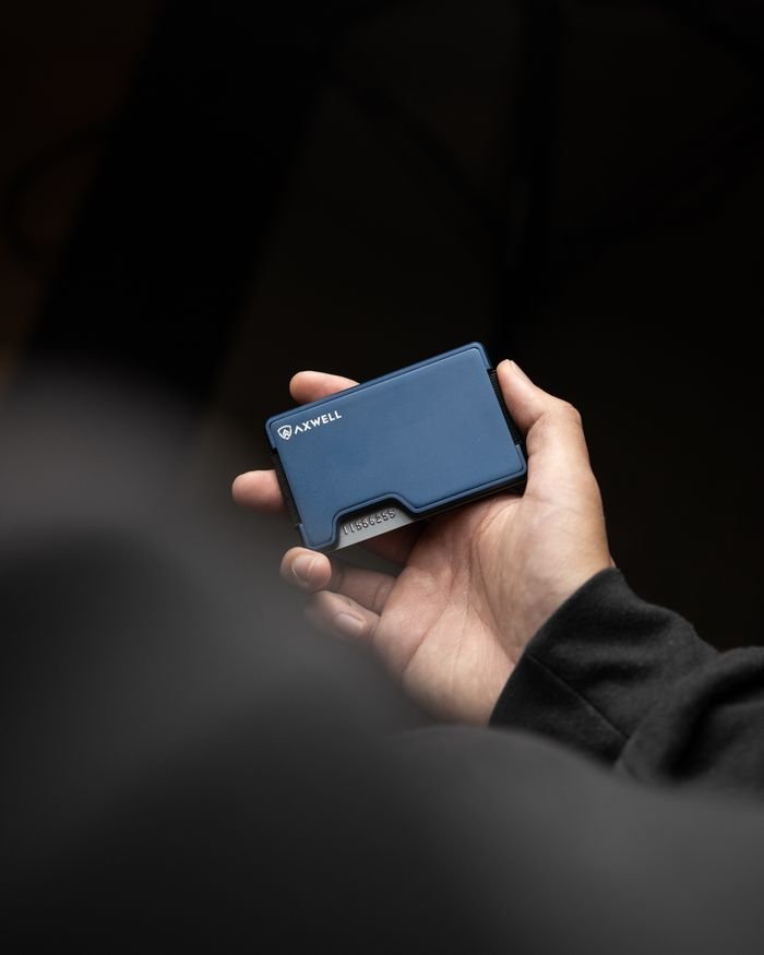 A person's hand holding a sleek, blue wallet against a dark background.